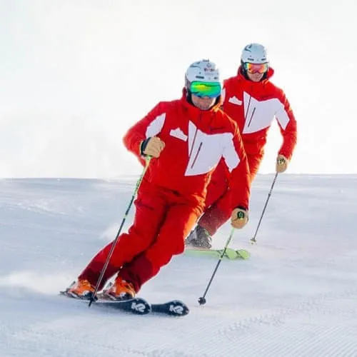 Zwei Skifahrer in roten Anzügen fahren über den Schnee