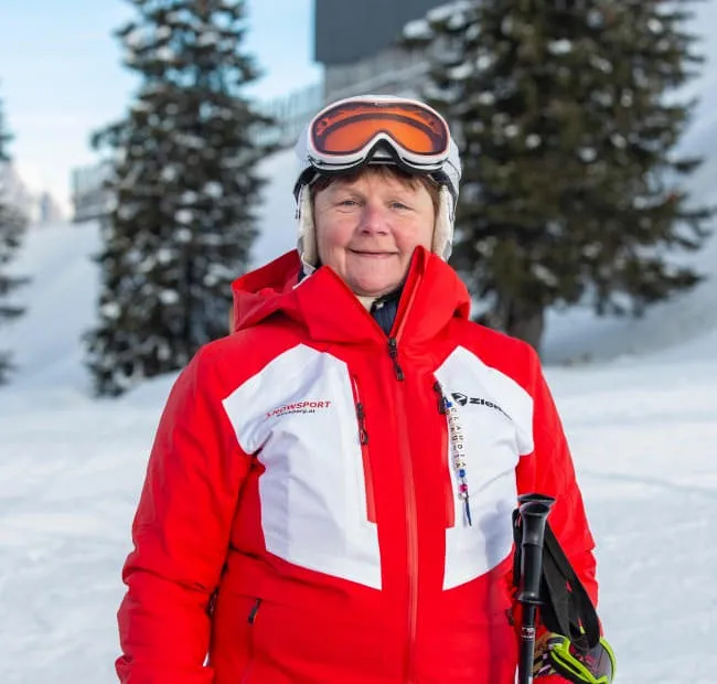 Frau in roter Skijacke mit Skiern im Schnee