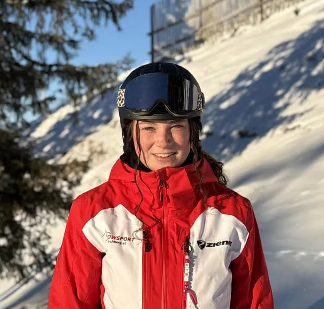 Lächelnde Skifahrerin in roter Jacke vor Schneegebiet