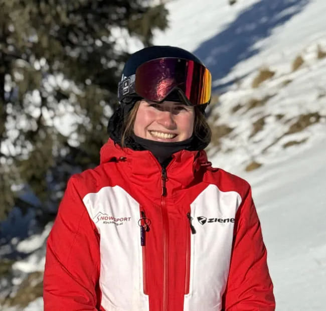 Lächelnde Skifahrerin in roter Jacke im Schnee