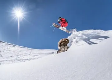Skifahrer springt über einen Hund im Schnee.